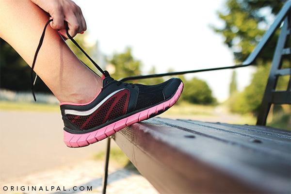 ورزشکاری در حال بستن بند کفش مخصوص دویدن مشکی بر روی صندلی پارک