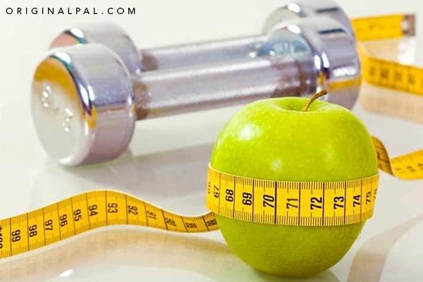 دو دمبل در کنار یک سانتی متر به دور یک سیب سبز به عنوان راه‌های کاهش وزن