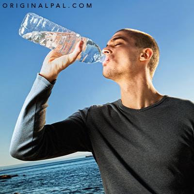 مردی در حال نوشیدن آب با باطری در کنار دریا